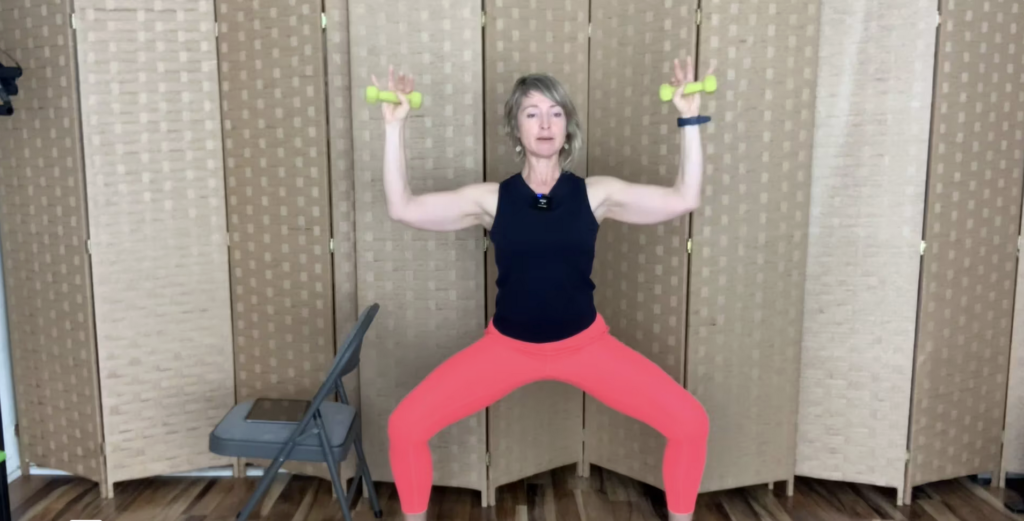 Woman standing in a deep plie position doing Pilates, barre and strength exercises holding weights in her arms.