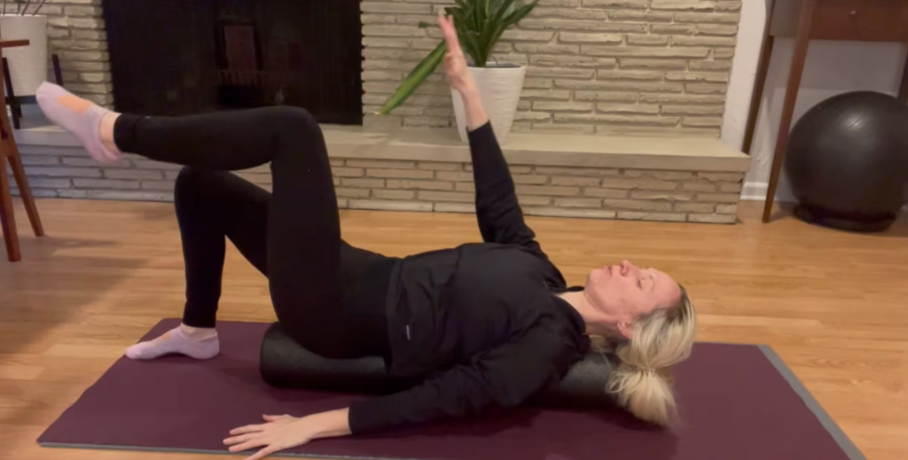 Woman lying on a foam roller on a Pilates mat doing exercises.