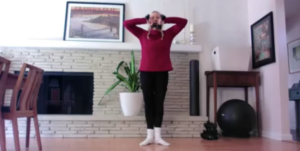 Woman doing standing arm exercises holding weights. The weights are making a heart.