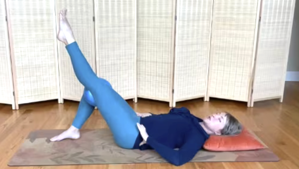 Woman lying on a Pilates mat doing exercises with one leg extended.