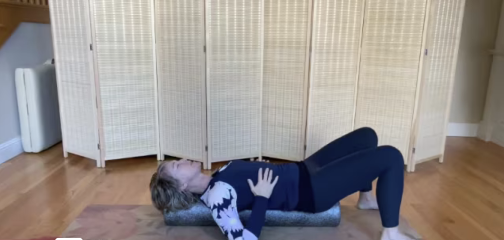 Woman lying on a foam roller on a Pilates mat doing exercises.