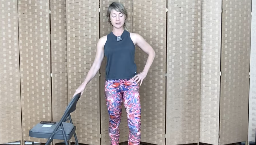 Woman standing doing exercises with a chair.