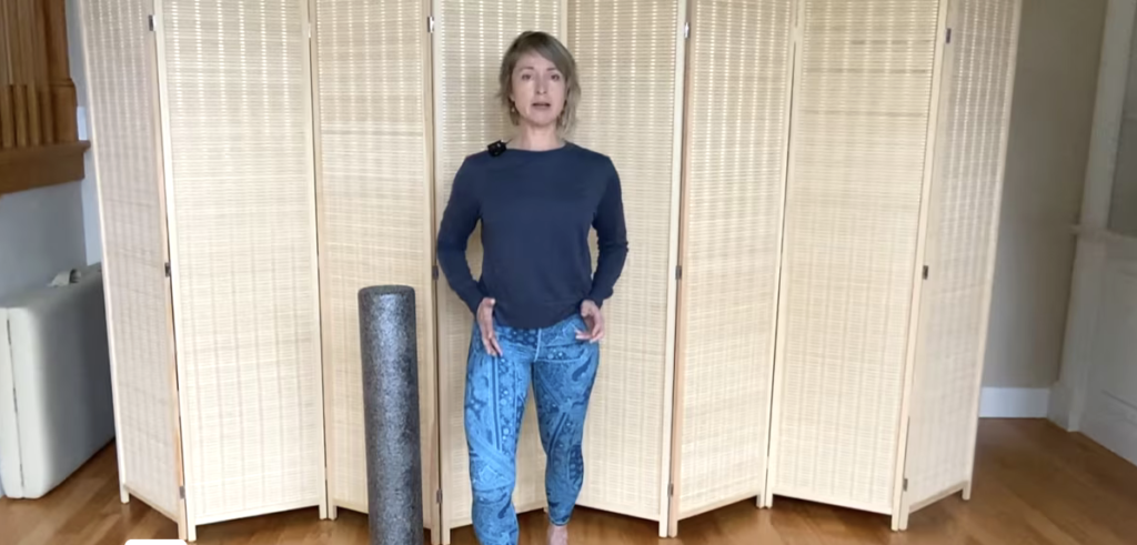 Woman standing doing PIlates exercises next to a foam roller.