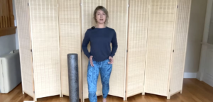 Woman standing doing PIlates exercises next to a foam roller.