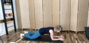 Woman doing a plank exercise with a loop band around her wrists on a PIlates mat.