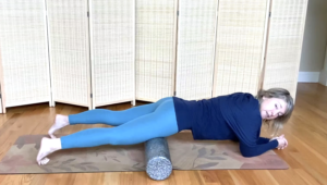 Woman on the floor with a Pilates mat rolling the front of her legs with a foam roller.