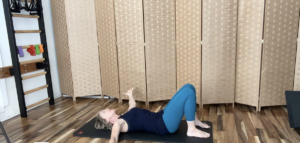 Woman lying on a Pilates mat doing Pilates exercises for her shoulders.