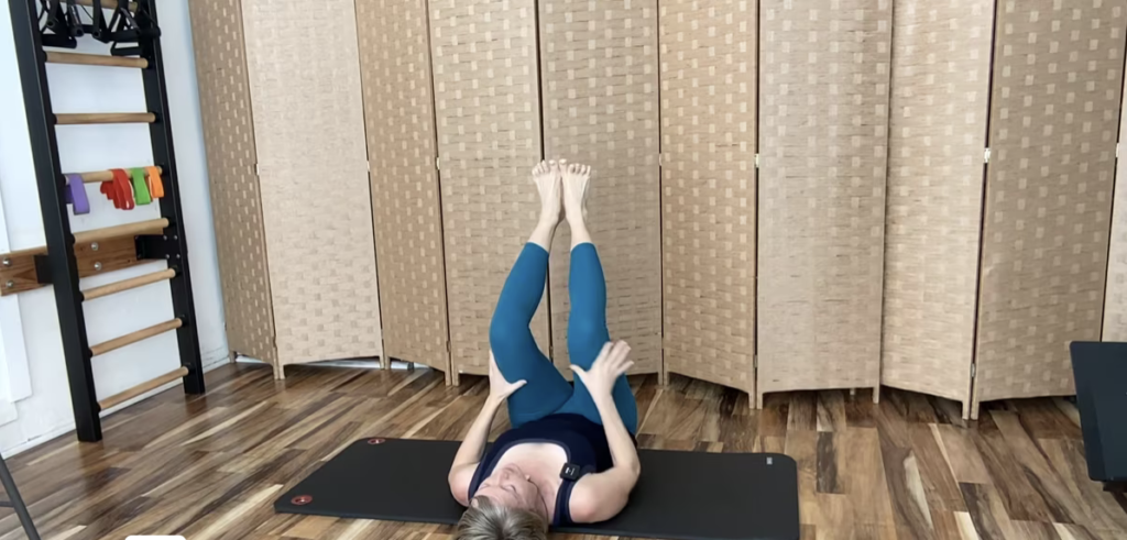 Woman doing Pilates exercises on a PIlates mat with her legs extended.