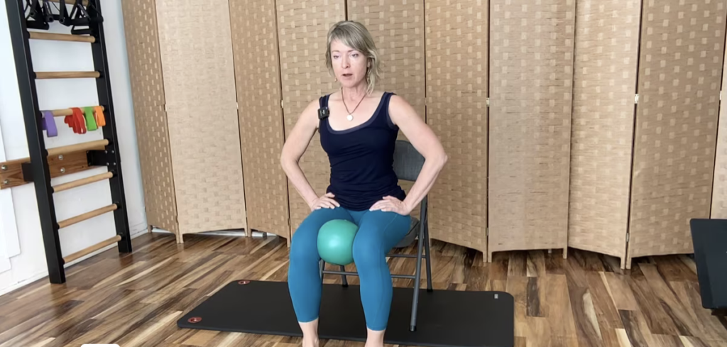 Woman seated on a chair with a ball between her knees doing Pilates exercises.