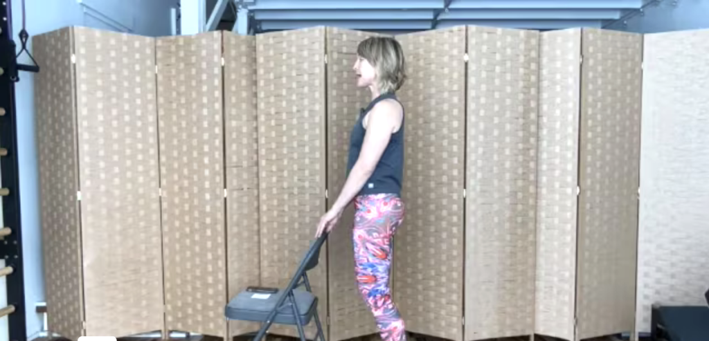 Woman standing holding on to a chair doing Pilates exercises.