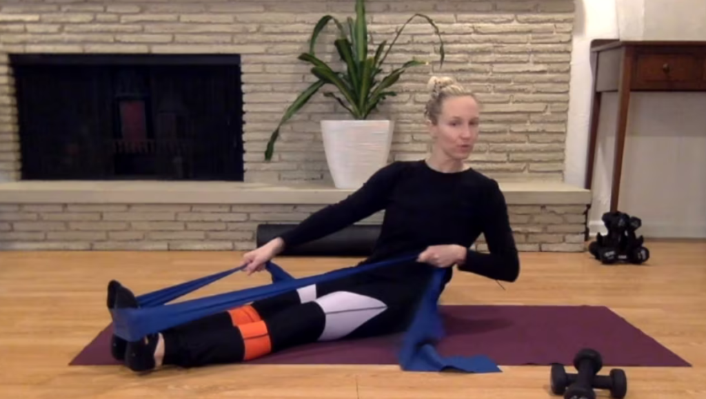 Woman doing Pilates abdominal and arm exercises with theraband on the mat