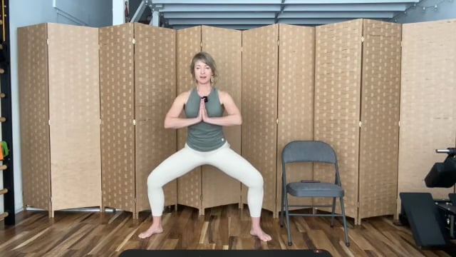 Woman doing Pilates squat exercises on the mat with hands pressed together