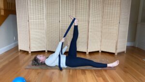 Woman doing Pilates exercises on the floor with band for stretching hamstring muscles