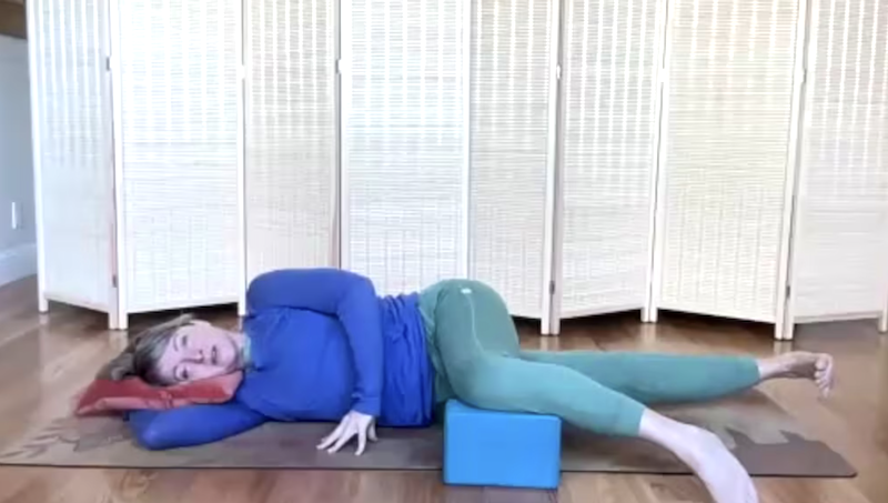 Woman doing Pilates exercises on the mat lying on her side. Her bottom leg is lifted and her top leg is on a yoga block.