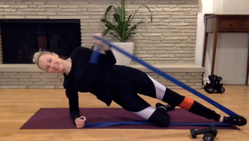 Woman doing Pilates abdominal and arm exercises with theraband on the mat