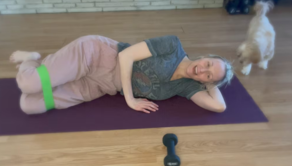 Woman lying on floor doing Pilates exercises with a dog