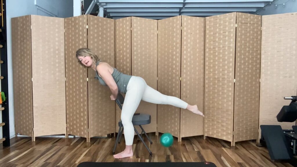 Woman doing Pilates exercises standing with a chair extending one leg for fitness strength and balance