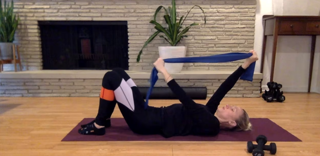 Woman doing Pilates abdominal and arm exercises with theraband on the mat