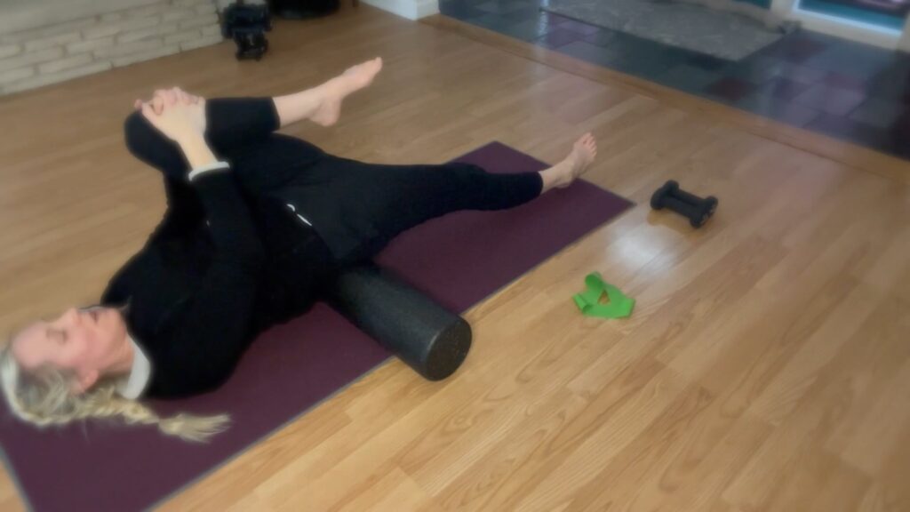 Woman doing Pilates on a Pilates mat with a foam roller.