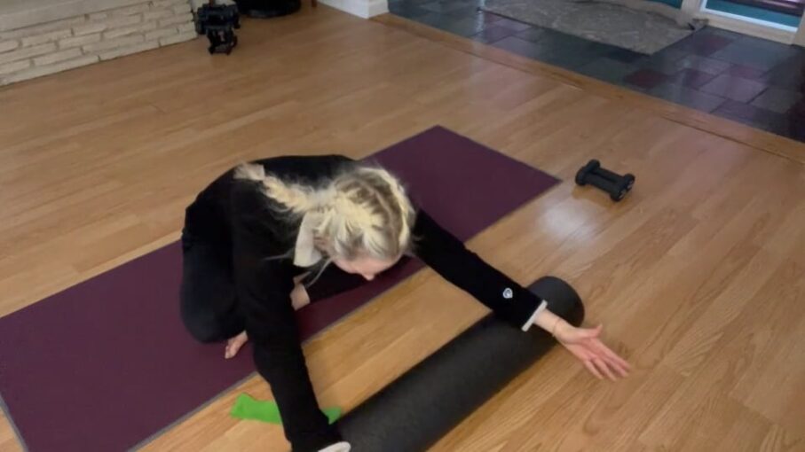 Woman doing Pilates exercises on a Pilates mat. She is sitting cross legged and stretching forward.