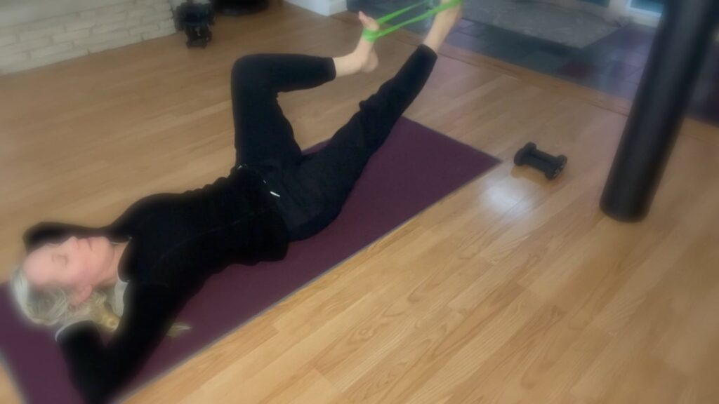 Woman doing Pilates on Pilates mat. She is using a loop band and her hands are behind her head.