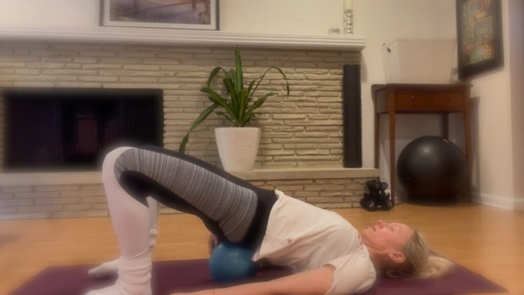 Woman doing Pilates with a ball on the yoga mat.