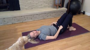 Woman doing Pilates on a mat with a dog and weights.