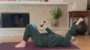 Woman doing Pilates exercises with weights on the floor.